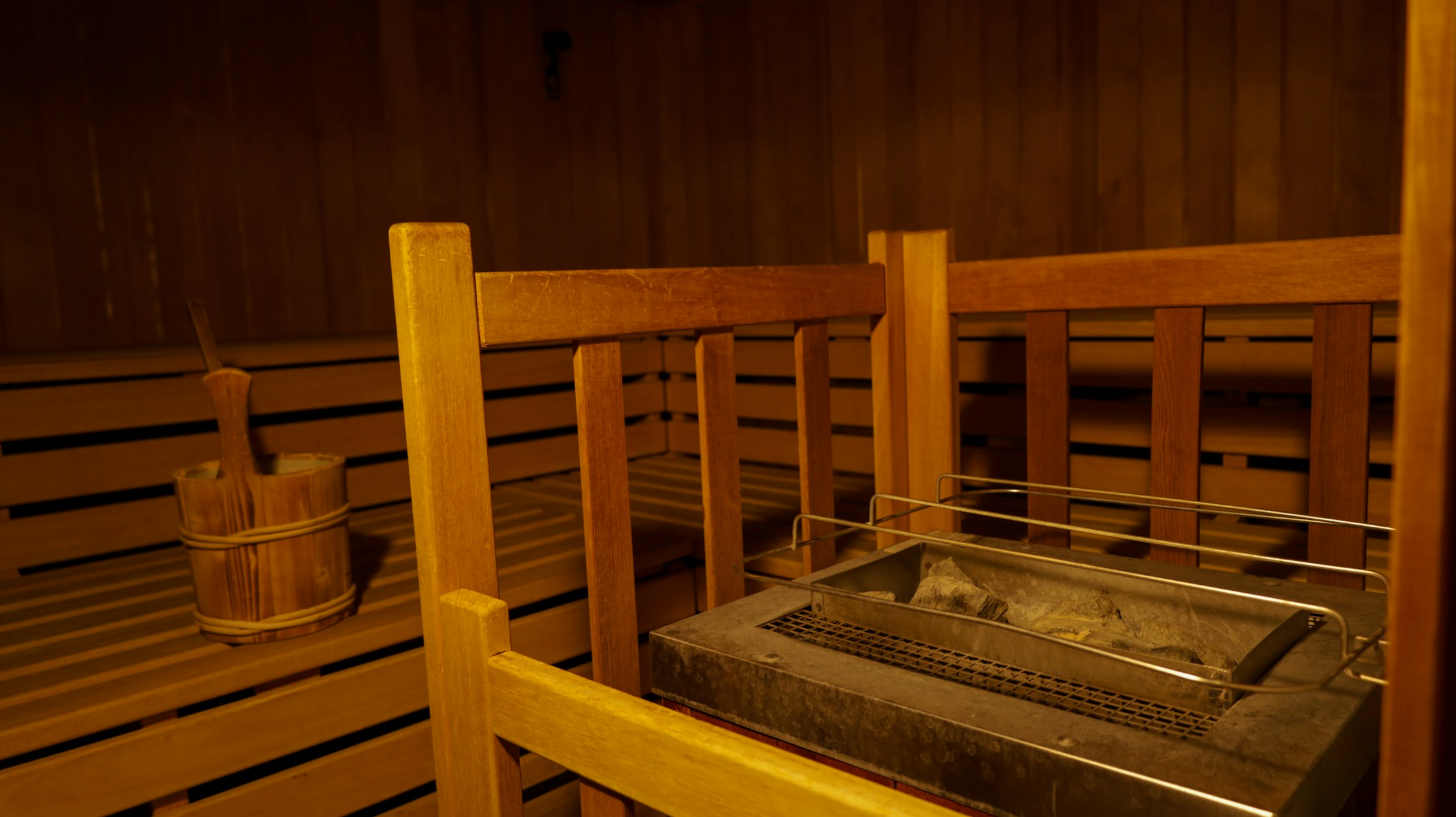Warm wooden sauna interior with a heater, stones, bucket, and ladle